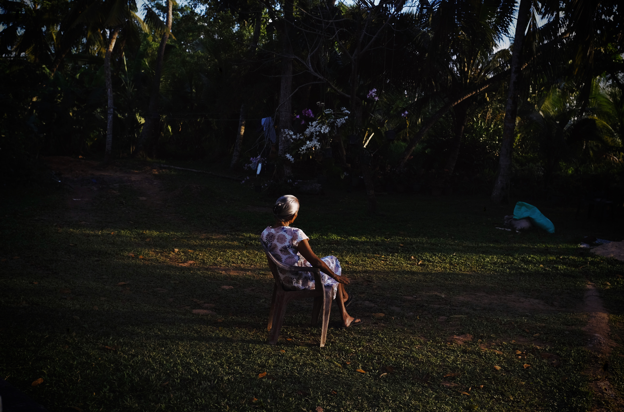 Sri Lanka, Weligama, 2021-10-24. An elder woman sitting on a chair in her garden by the end of the day. Photograph by Noemie de Bellaigue / Hans Lucas. 
Sri Lanka, Weligama, 2021-10-24. Une femme agee assise sur une chaise dans son jardin en fin de journee. Photographie par Noemie de Bellaigue / Hans Lucas.